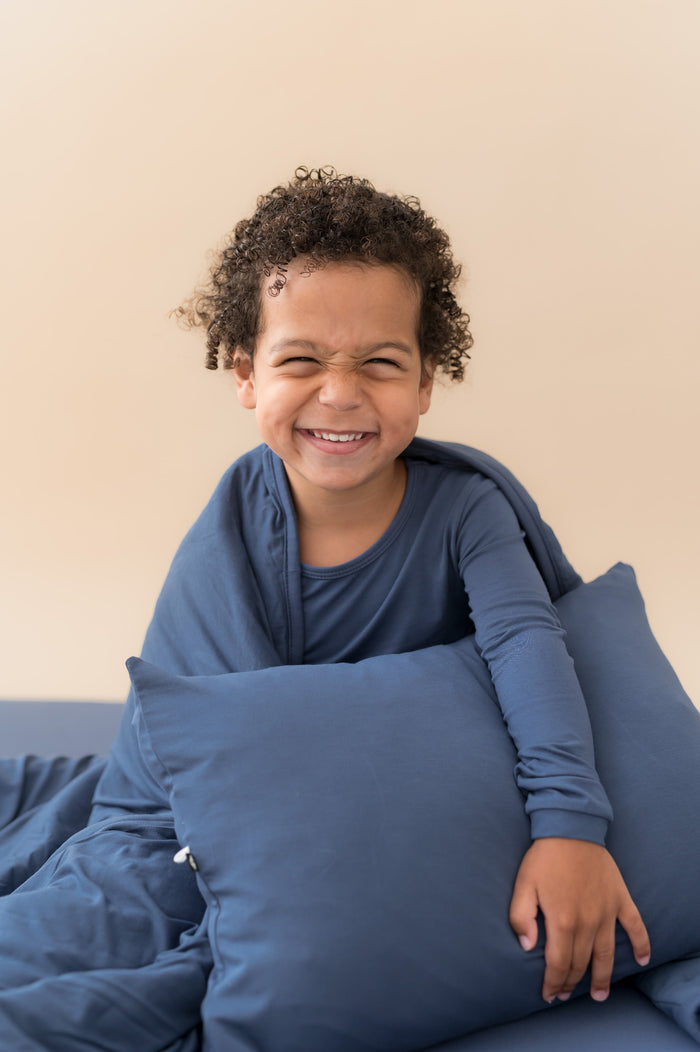 Boy holding Toddler Pillowcase in Oxford sitting with similar color blanket and wearing Oxford shirt