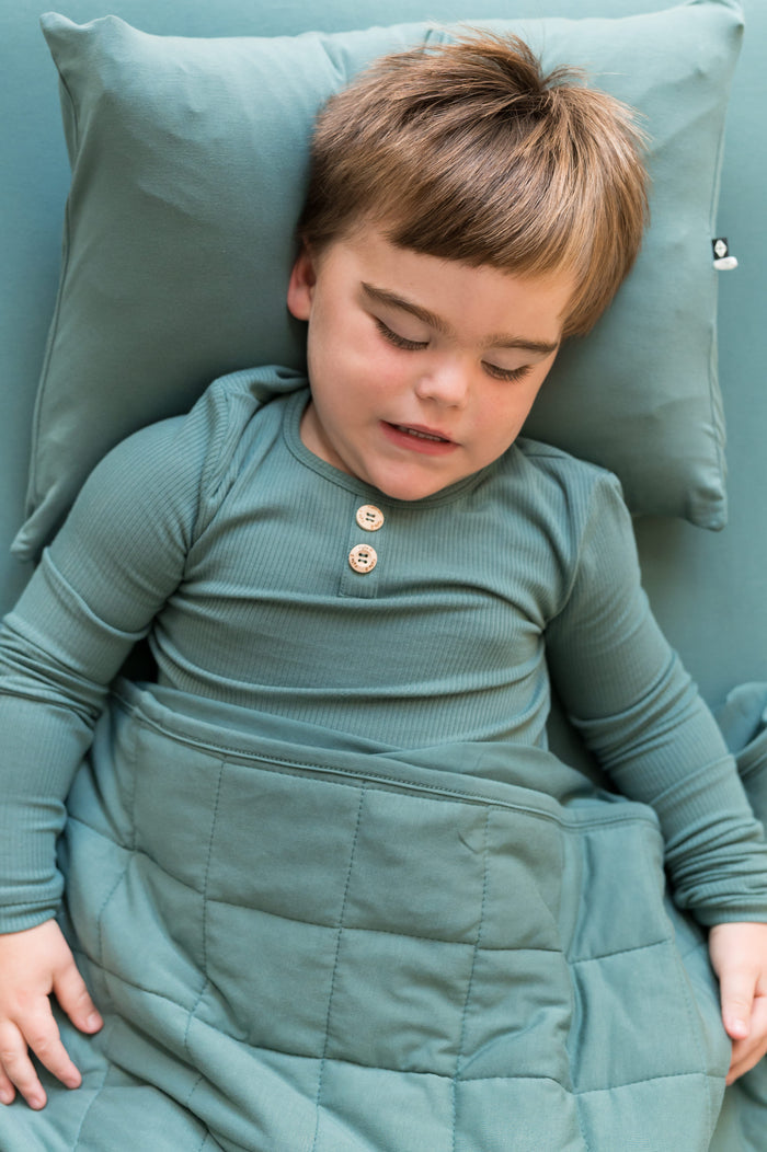 Boy sleeping on Toddler Pillowcase in Pine while wearing Pine color shirt covered under pine color blanket