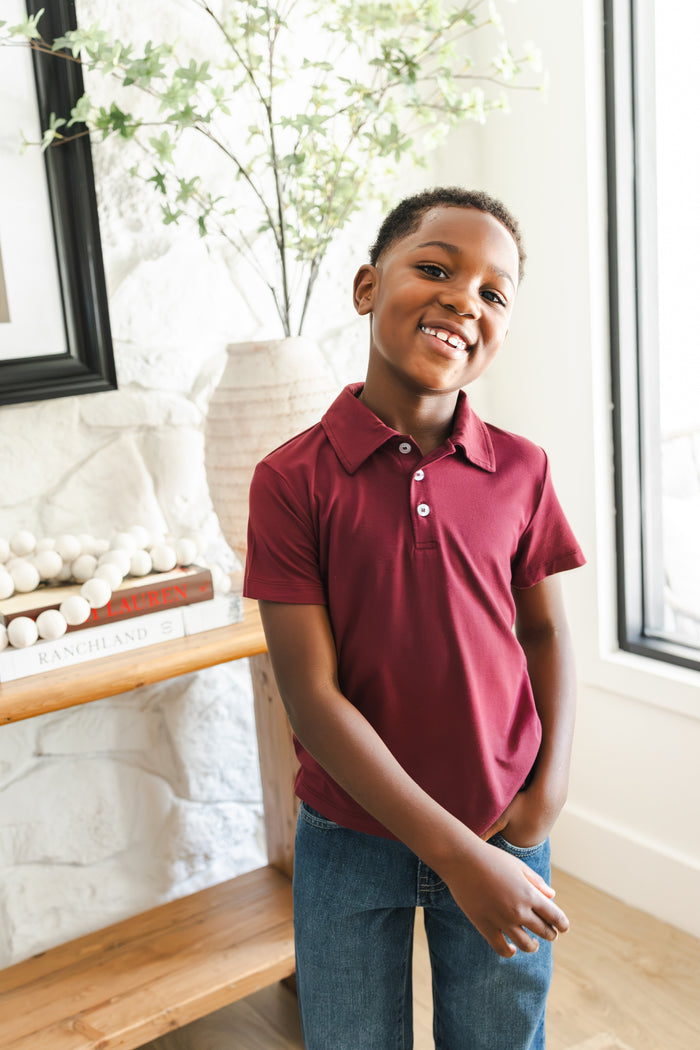 Boy smiling in Toddler Short Sleeve Polo in Burgundy on blue jeans