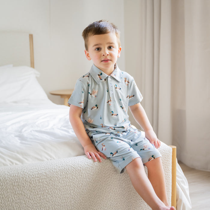 Young bow sitting on the edge of a bed wearing the Toddler Short Sleeve Polo in Mallard Duck with matching drawstring shorts