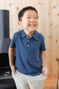 Toddler smiling in Toddler Short Sleeve Polo in Oxford over white pants