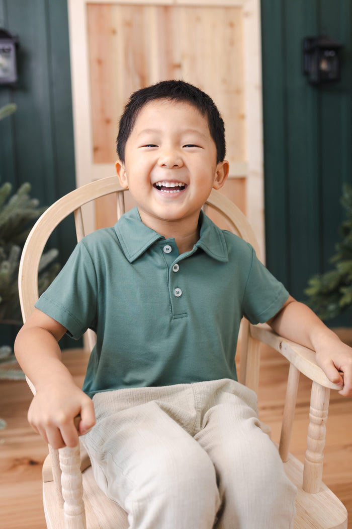 Toddler sitting on a chair wearing Toddler Short Sleeve Polo in Pine over off white pants