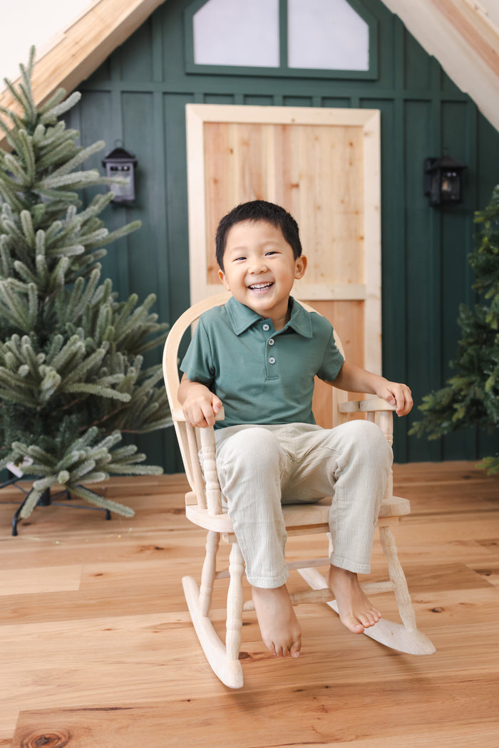 Toddler sitting on a chair wearing Toddler Short Sleeve Polo in Pine over off white pants