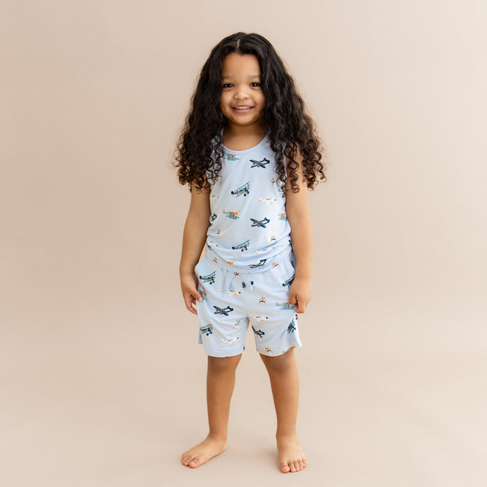 Young girl standing in front of a light beige background wearing the Toddler Tank Top in Take Off with matching drawstring shorts