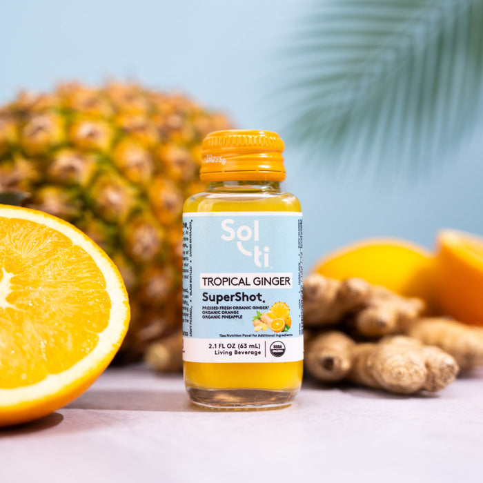 Sol-ti TROPICAL GINGER SuperShot glass bottle next to orange slices, ginger root, and pineapple