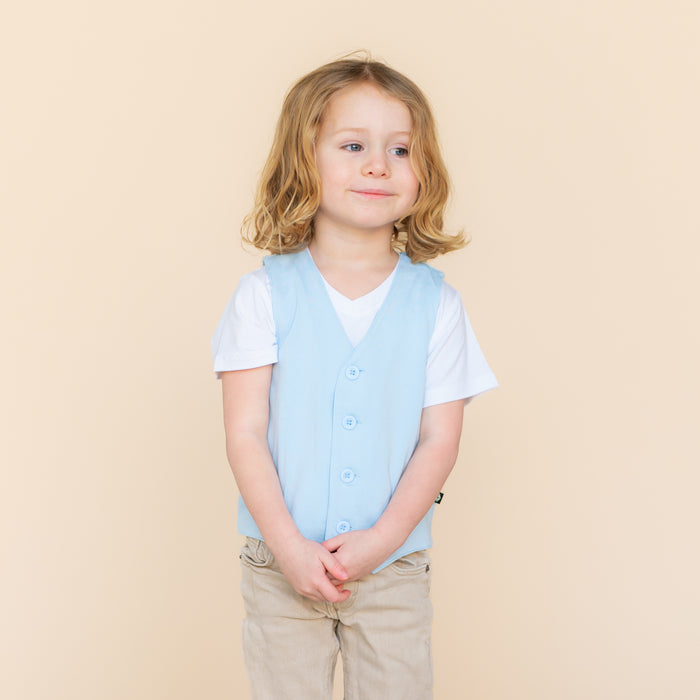 Young model wearing the Tuxedo Vest in Breeze over top of a white vneck paired with khaki pants