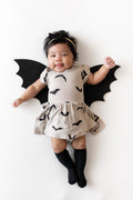 Baby wearing Twirl Bodysuit Dress in Bats print with bat wings and black socks on a white background