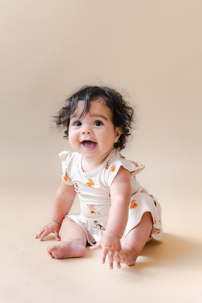 Baby posing in Twirl Bodysuit Dress in Halloween Teddy print on a beige background