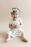 Child wearing a green and white striped twirl bodysuit dress with colorful Harry Potter patterns and a green headband on a beige background