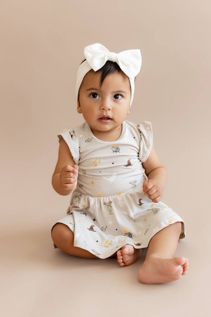 Child wearing a Harry Potter patterned twirl bodysuit dress with a white bow headband on a beige background