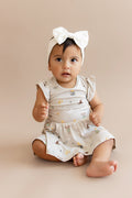 Child wearing a Harry Potter patterned twirl bodysuit dress with a white bow headband on a beige background