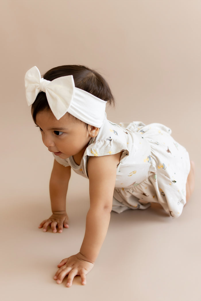 Child crawling wearing a Harry Potter patterned twirl bodysuit dress with a white bow headband on a beige background
