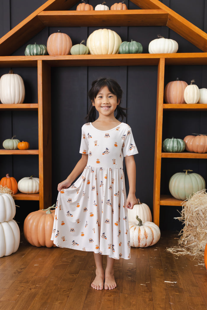 Girl wearing Twirl Dress in Halloween Teddy print standing in front of pumpkin Halloween decorations around