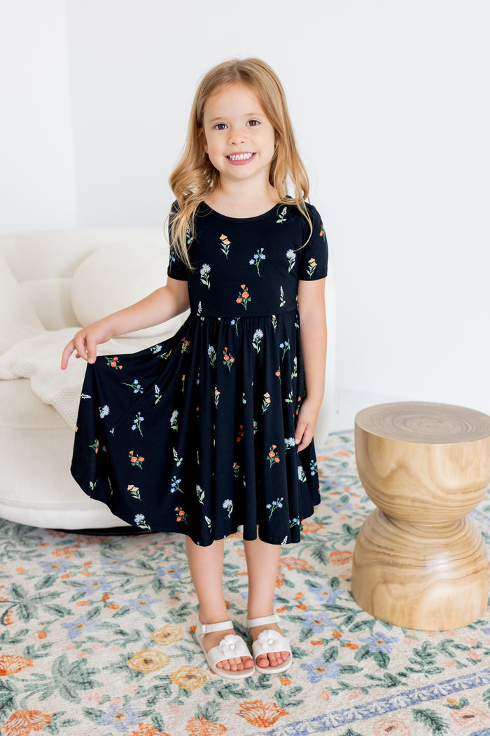 Girl posing in Twirl Dress in Midnight Wildflower print and white sandals standing in a living room