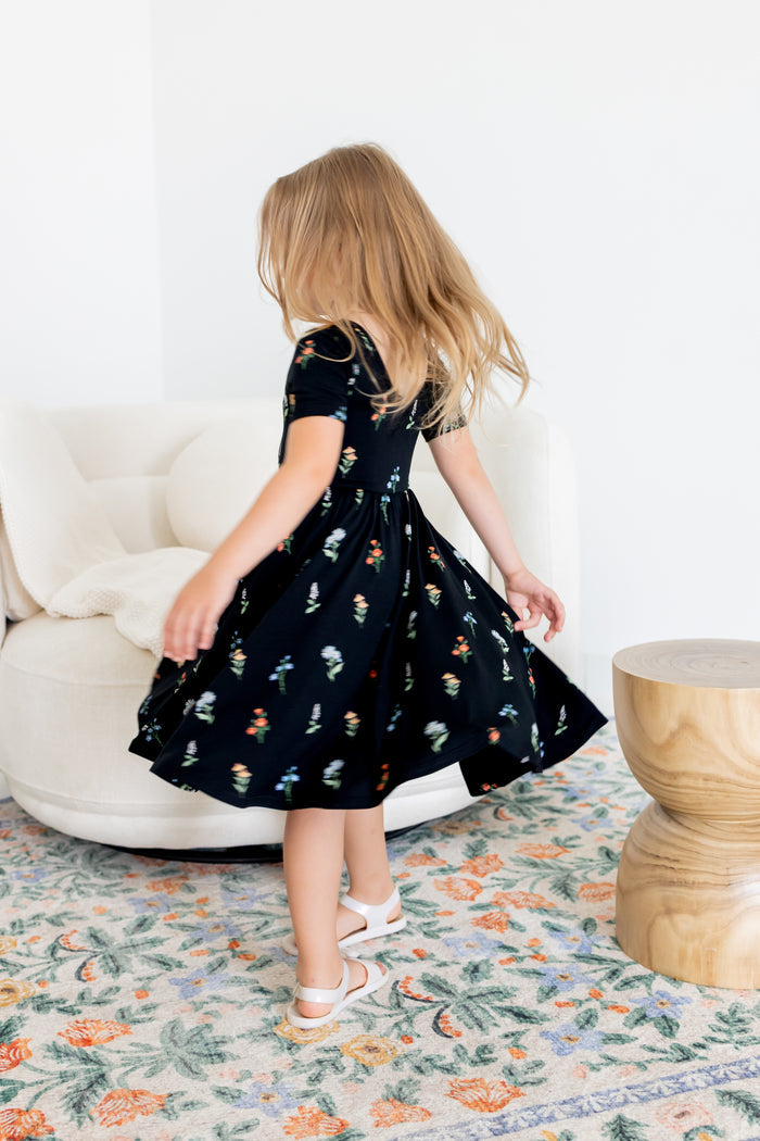 Girl twirling in Twirl Dress in Midnight Wildflower print and white sandals standing in a living room