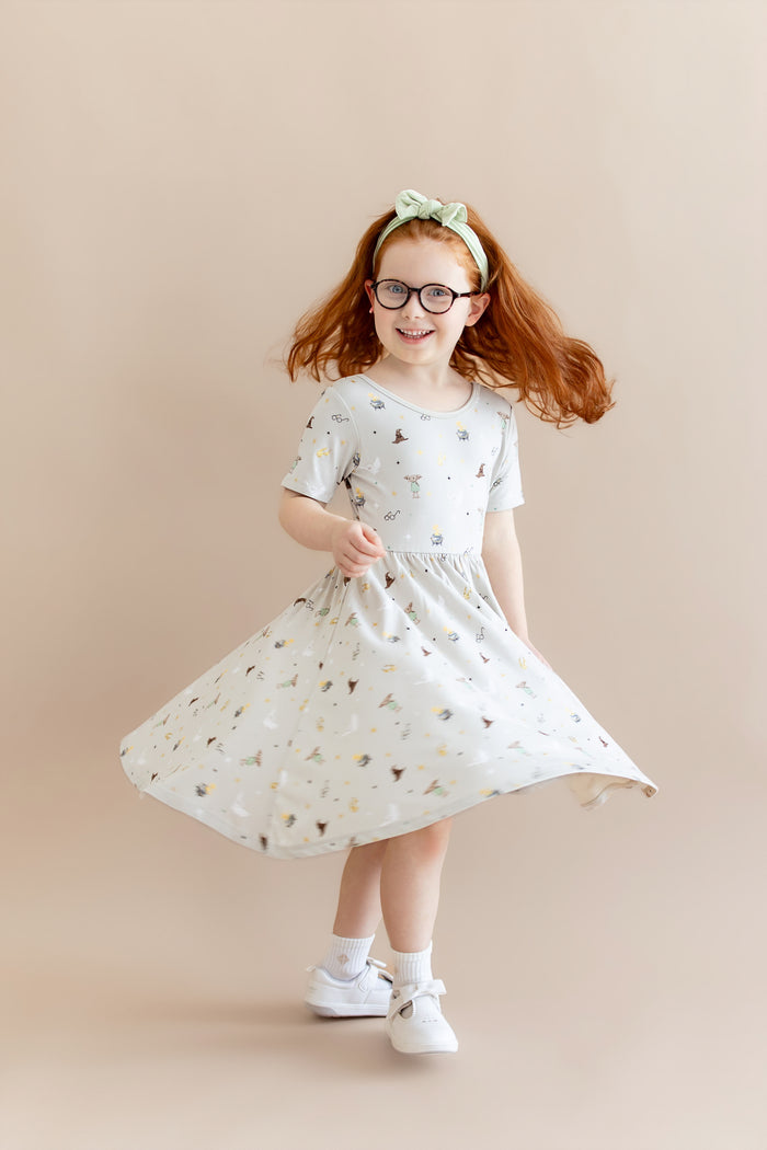 Child twirling in a Harry Potter patterned twirl dress with a green headband and white socks and shoes on a beige background