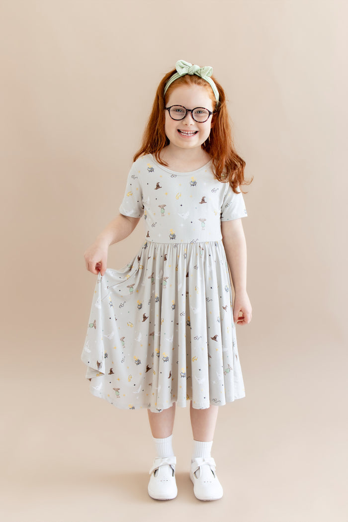 Child wearing a cream Twirl dress with Harry Potter prints with white socks and shoes and green headband on a beige background