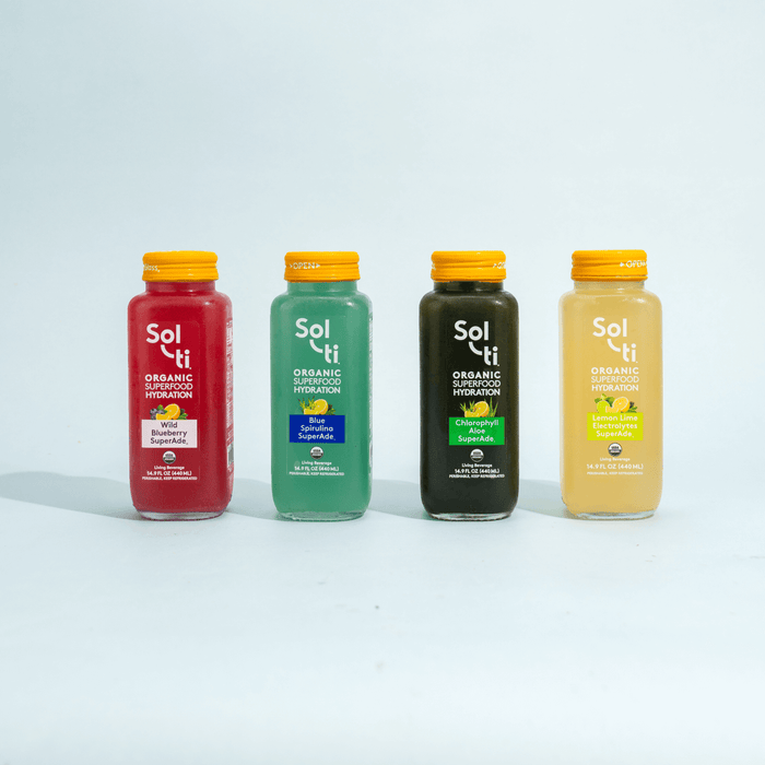Four glass SuperAde bottles: Chlorophyll Aloe, Blue Spirulina, Lemon Lime & Wild Blueberry