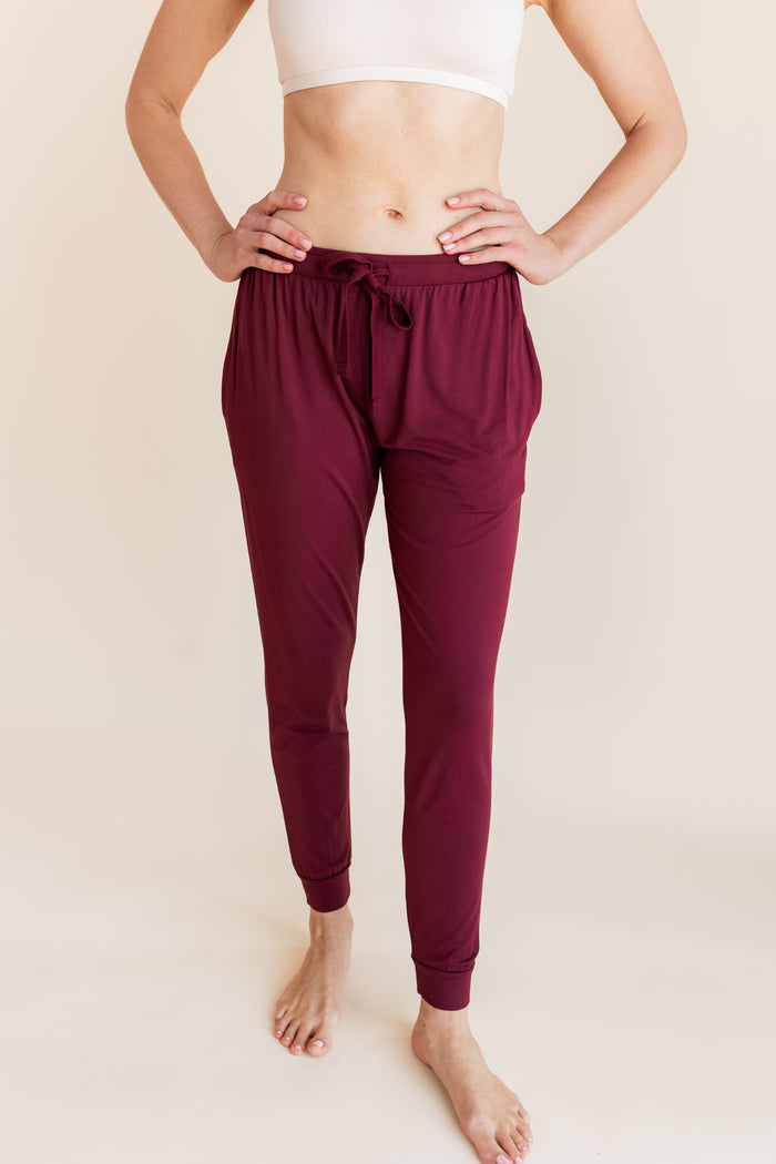 Model wearing Women's Jogger Pants in Burgundy under white bralette on a beige background