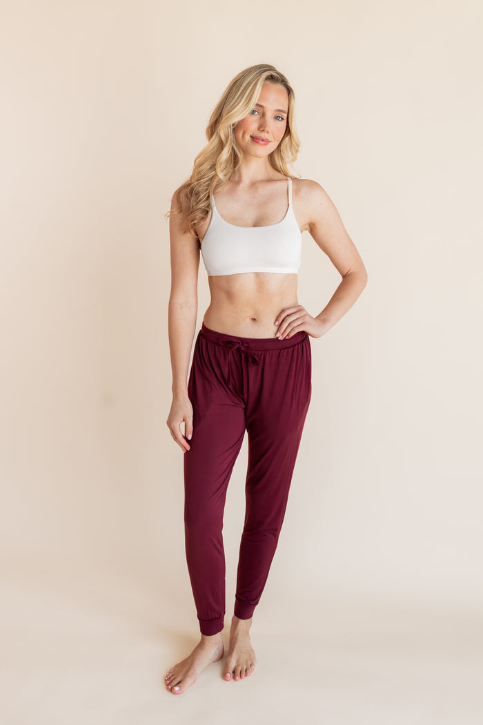 Model posing in Women's Jogger Pants in Burgundy under white bralette on a beige background