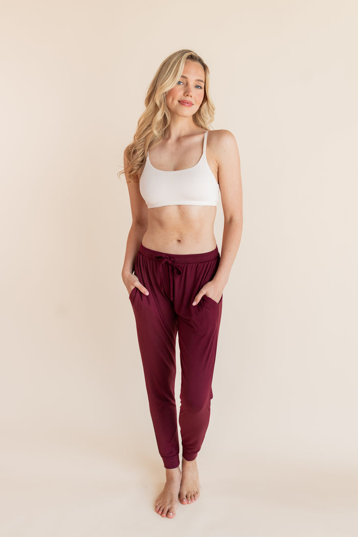 Model wearing Women's Jogger Pants in Burgundy with pockets under white bralette on a beige background