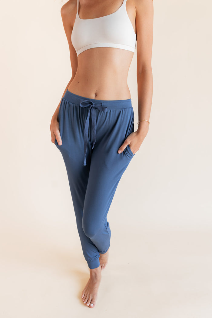 Close up of Model wearing Women's Jogger Pants in Oxford with pockets under a white bralette top on a beige background