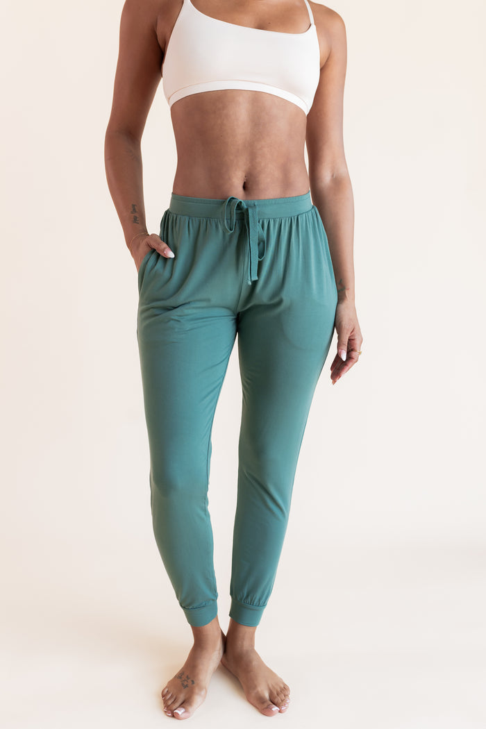 Model wearing Women's Jogger Pants in Pine under white bralette on a beige background
