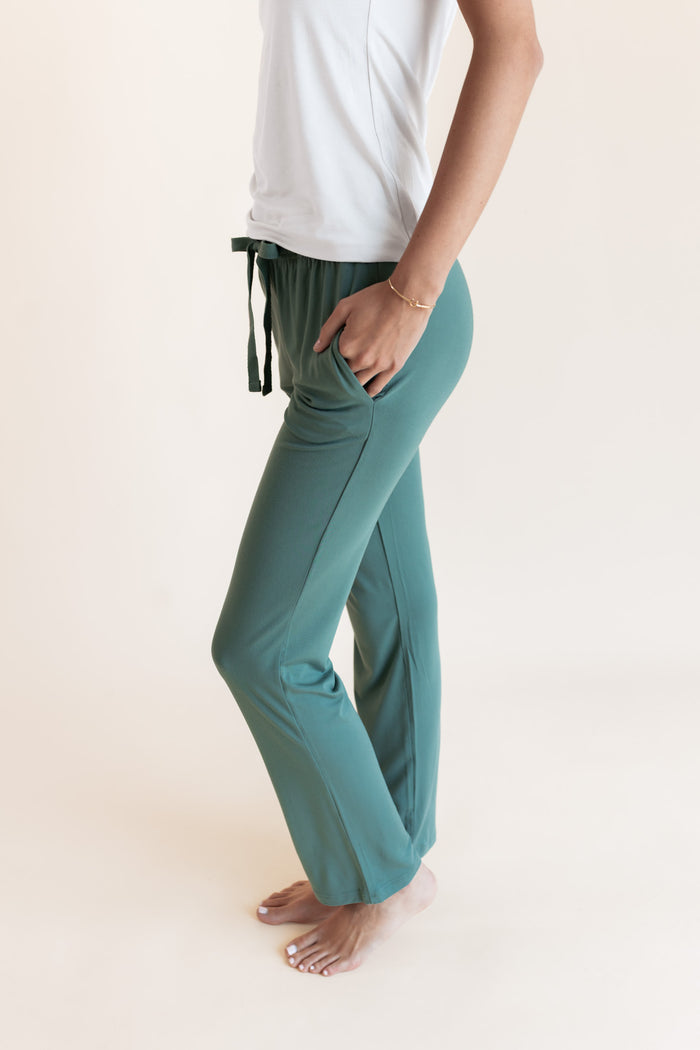 Model showcasing Women's Lounge Pants in Pine with pockets under white camisole on a beige background
