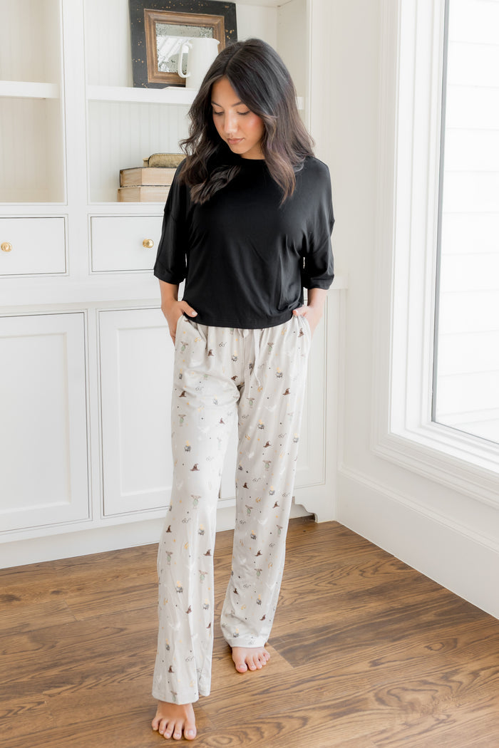 Model standing in a room wearing a cream lounge pant with pockets having Harry Potter prints with a black t-shirt