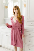 Female standing in a bathroom wearing the Women’s Lounge Robe in Apple Blossom holding the tied waistband