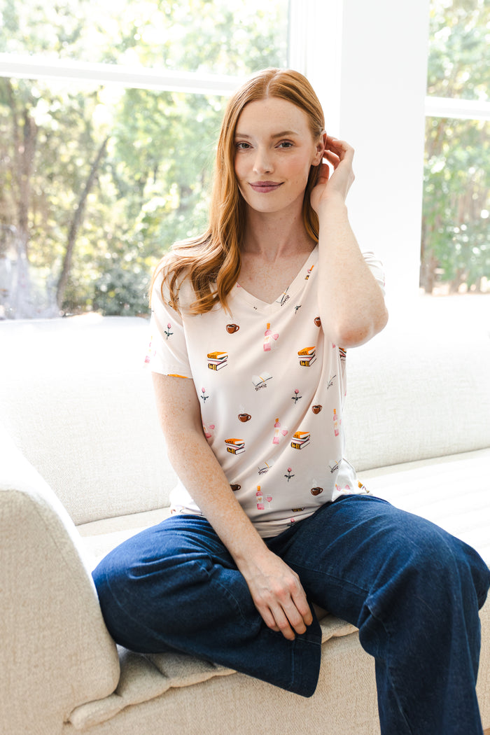 Modal wearing Women's Relaxed Fit V-Neck in Book Club print over blue jeans sitting on white sofa
