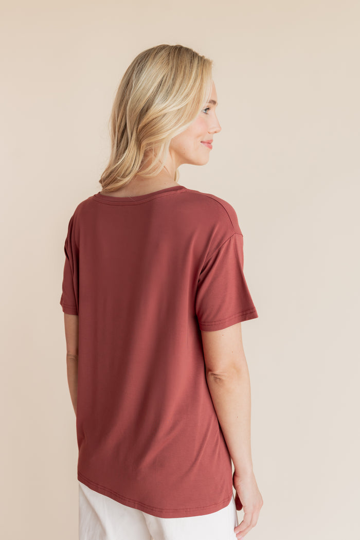 Model showcasing backside of Women's Oversized V-Neck Tee in Ember over white pants on a beige background