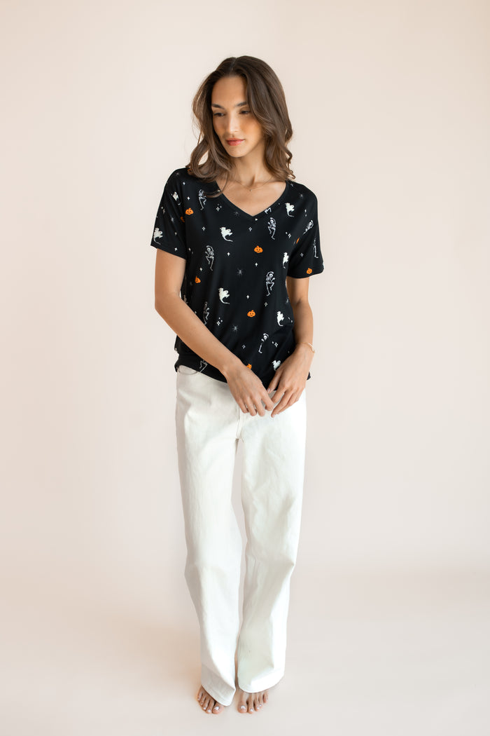 Modal posing in Women's Oversized V-Neck Tee in Halloween Friends print over white pants on a beige background