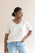 Woman wearing a cream t-shirt with colorful mickey patterns and light blue jeans against a beige background
