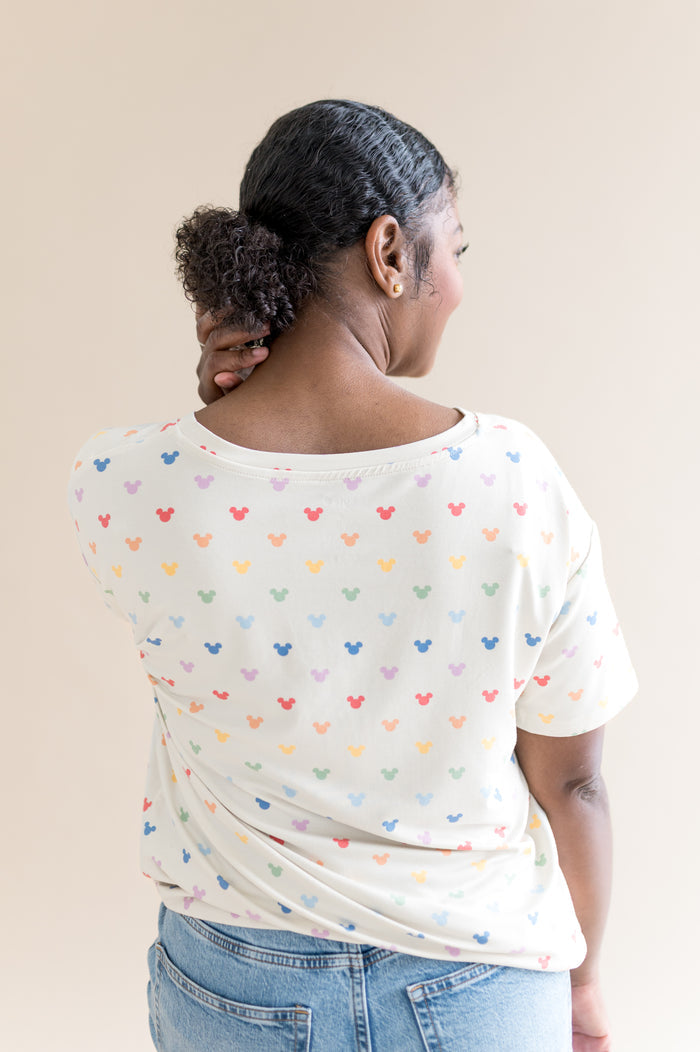 Person wearing a white t-shirt with colorful mickey patterns on a beige background