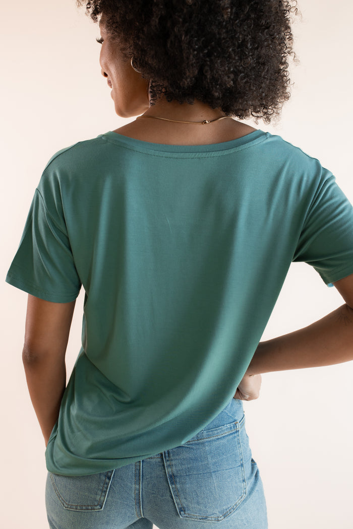 Model showcasing back side of Women's Oversized V-Neck Tee in Pine over blue jeans on a beige background