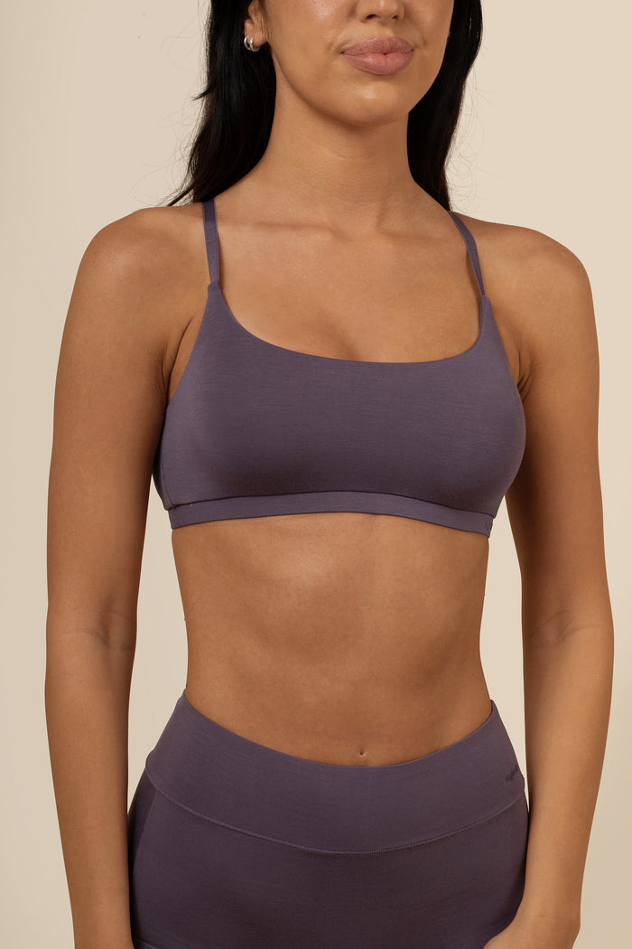 Person wearing a dark purple scoop bra and leggings on a beige background