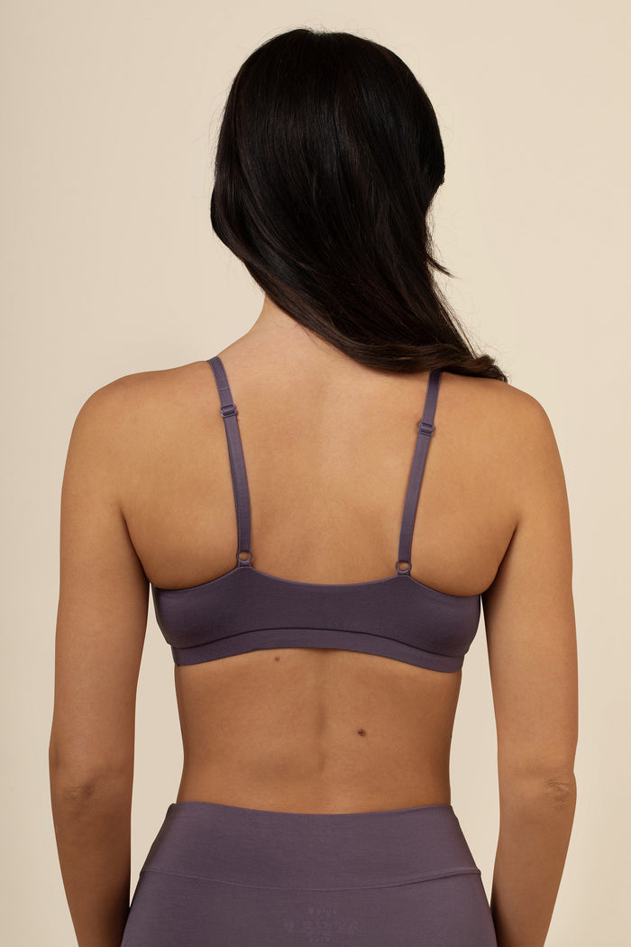 Woman wearing a purple sports bra and leggings on a beige background