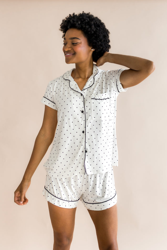 Model posing in Women's short sleeve pajama set in Midnight Polka Dot print with black piping on a beige background