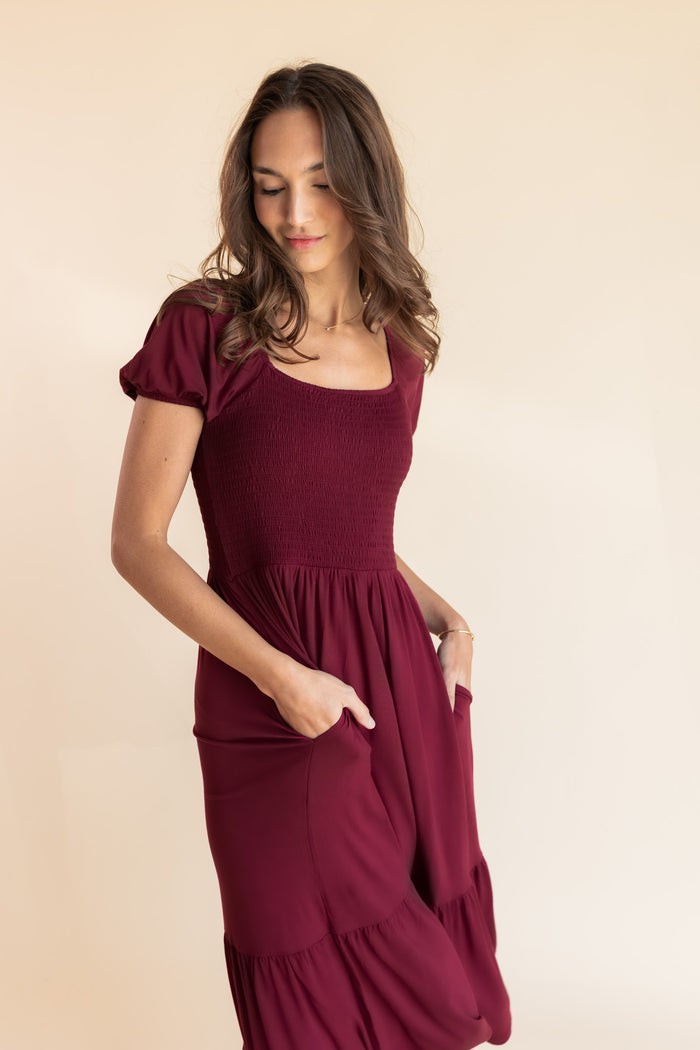 Model posing in Women’s Smocked Dress in Burgundy with pockets on a beige background
