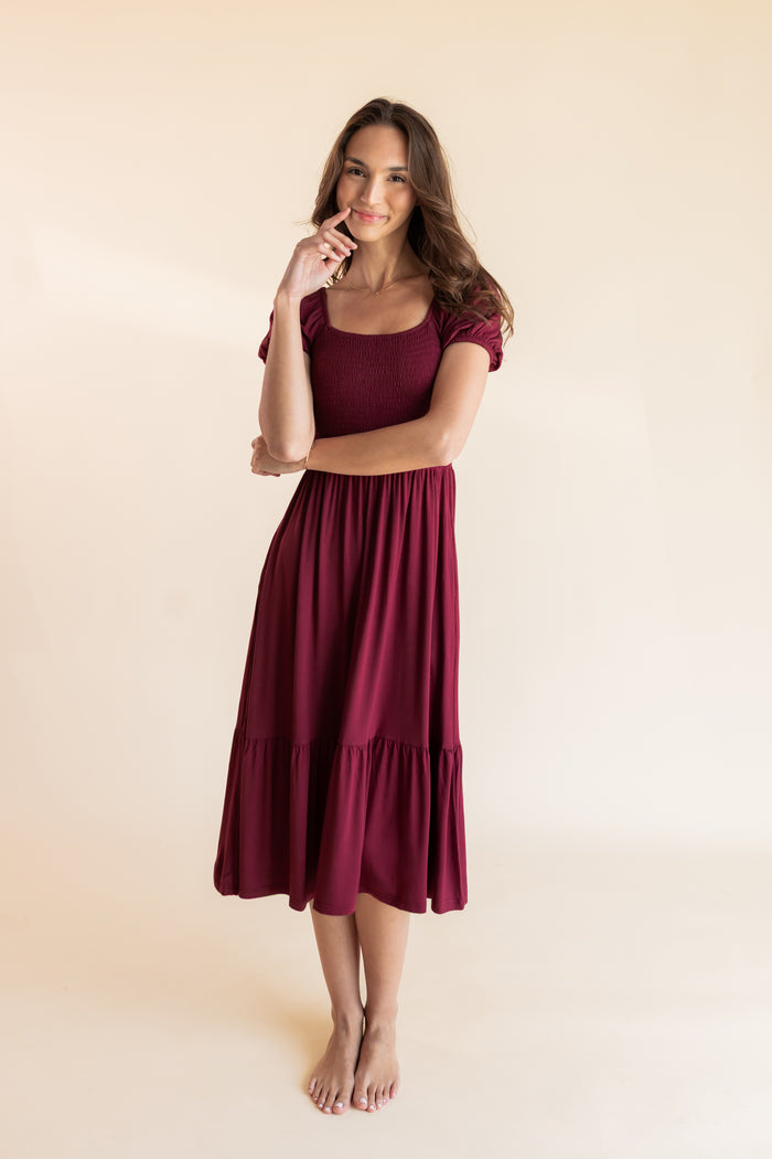 Model wearing Women’s Smocked Dress in Burgundy on a beige background