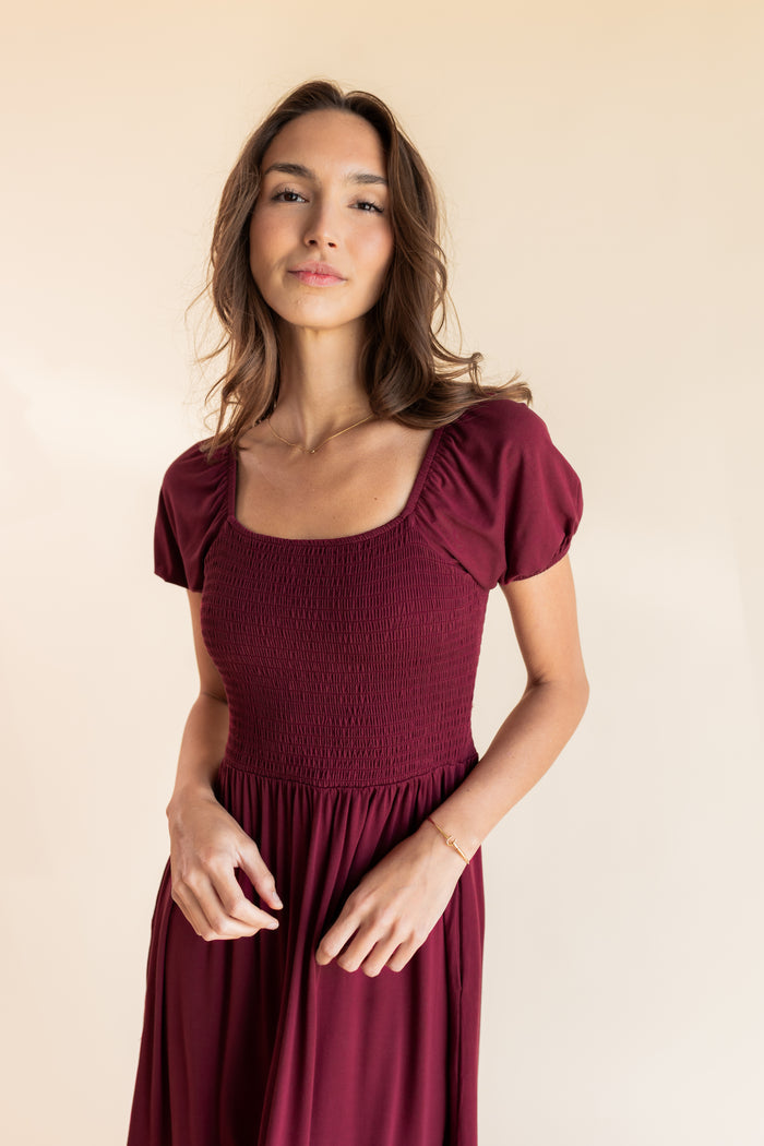 Model wearing Women’s Smocked Dress in Burgundy on a beige background