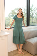 Model wearing Women’s Smocked Dress in Pine standing in a living room