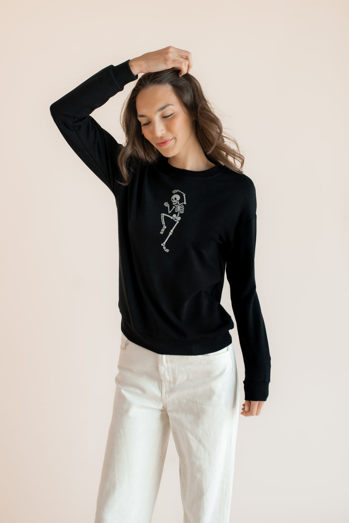 Modal posing in Black Women's Sweatshirt with Skeleton print in the center over white pants on a beige background