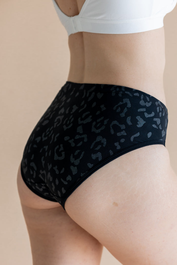 Person wearing black leopard patterned underwear on a beige background