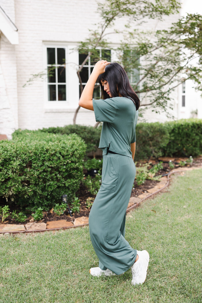Female model posing in a garden outdoors wearing the Women's Wide Leg Pant in Burgundy and matching short sleeve tee over white shoes