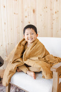 Child covered with Youth Blanket in Ochre 2.5 sitting on a sofa