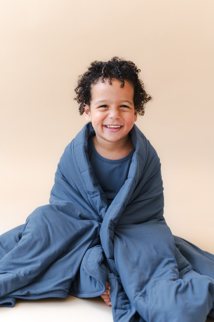 Boy sitting with Youth Blanket in Oxford 2.5 wrapped around him over the shoulders on a beige background