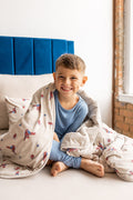 Boy sitting on a bed with oat color sheets and pillow wrapped in oat color Youth Blanket with Spider-Man print wearing blue pajamas
