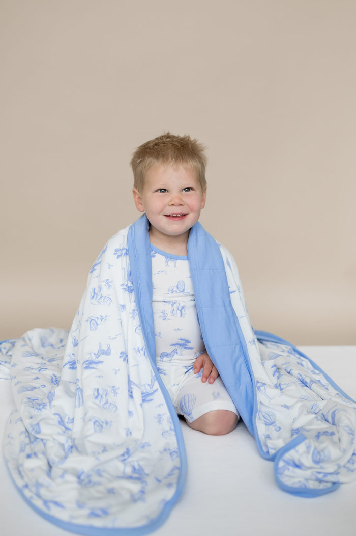 Young boy sitting on his knees with the Youth Blanket in Toile Safari 1.0 around his shoulders